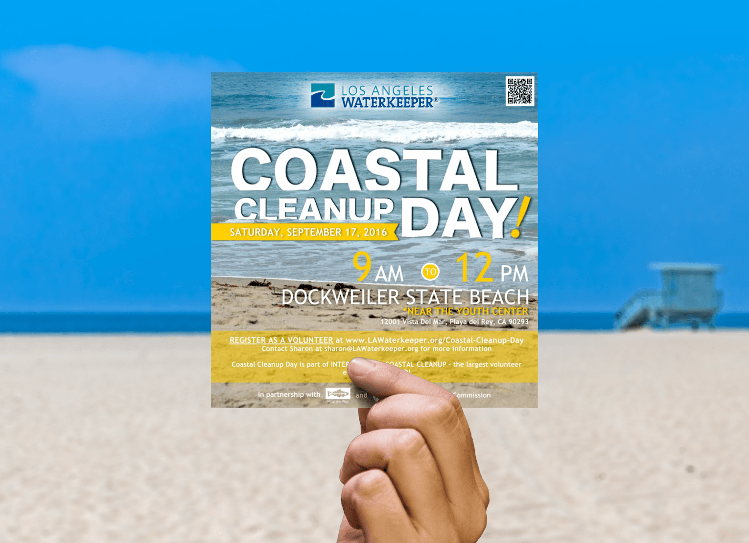 Hand holding up a Coastal Cleanup Day event flyer with the beach in the background.