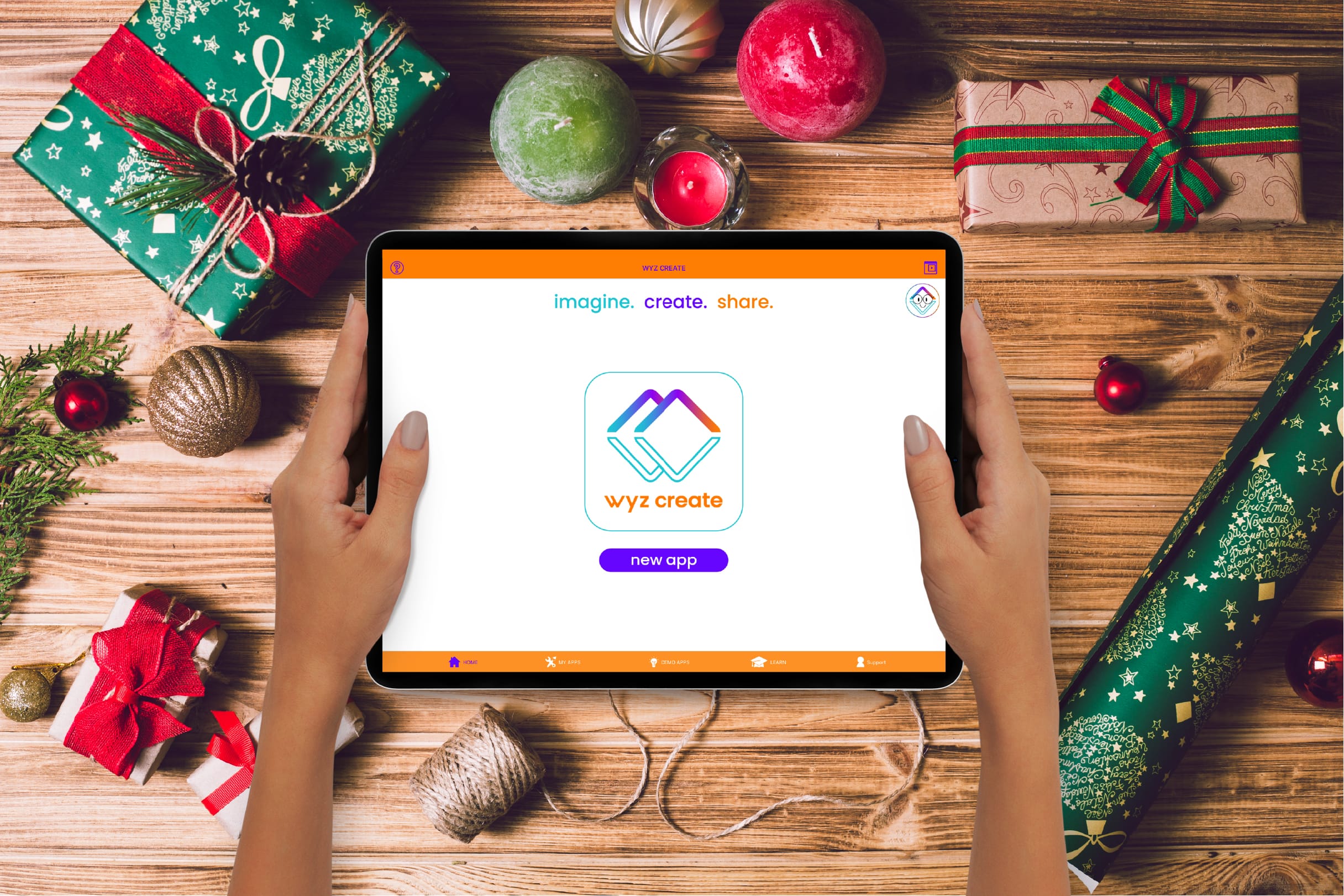 Holiday promotional image for Wyz Create featuring a pair of hands holding an ipad with the Wyz Create app home screen all above a table filled with ornaments and wrapping paper.